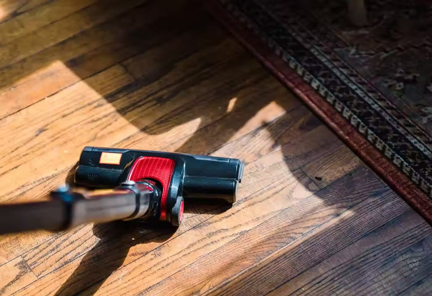 A vacuum on a hardwood floor beside a patterned rug