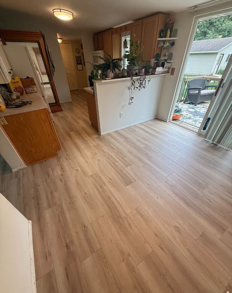Light wood-look luxury vinyl plank running from a kitchen into a living area, with a sliding door to a deck